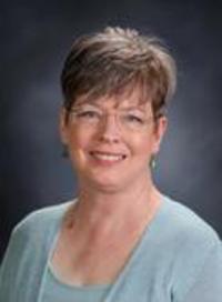 A woman with short hair and glasses is smiling.