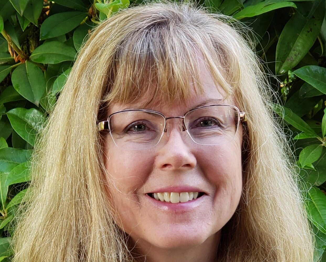 A woman with glasses and long hair is smiling.